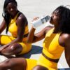 2 women in yellow and black bikini sitting on beach during daytime